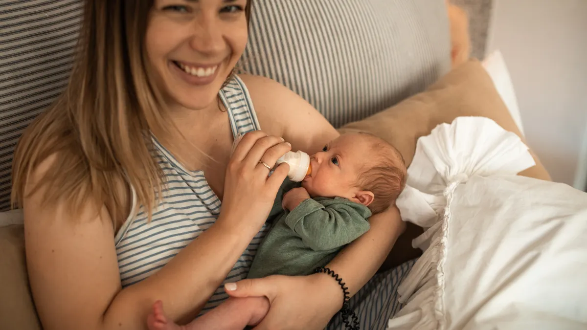 How to tell if your baby is getting enough milk Woman bottle-feeding an infant on a bed