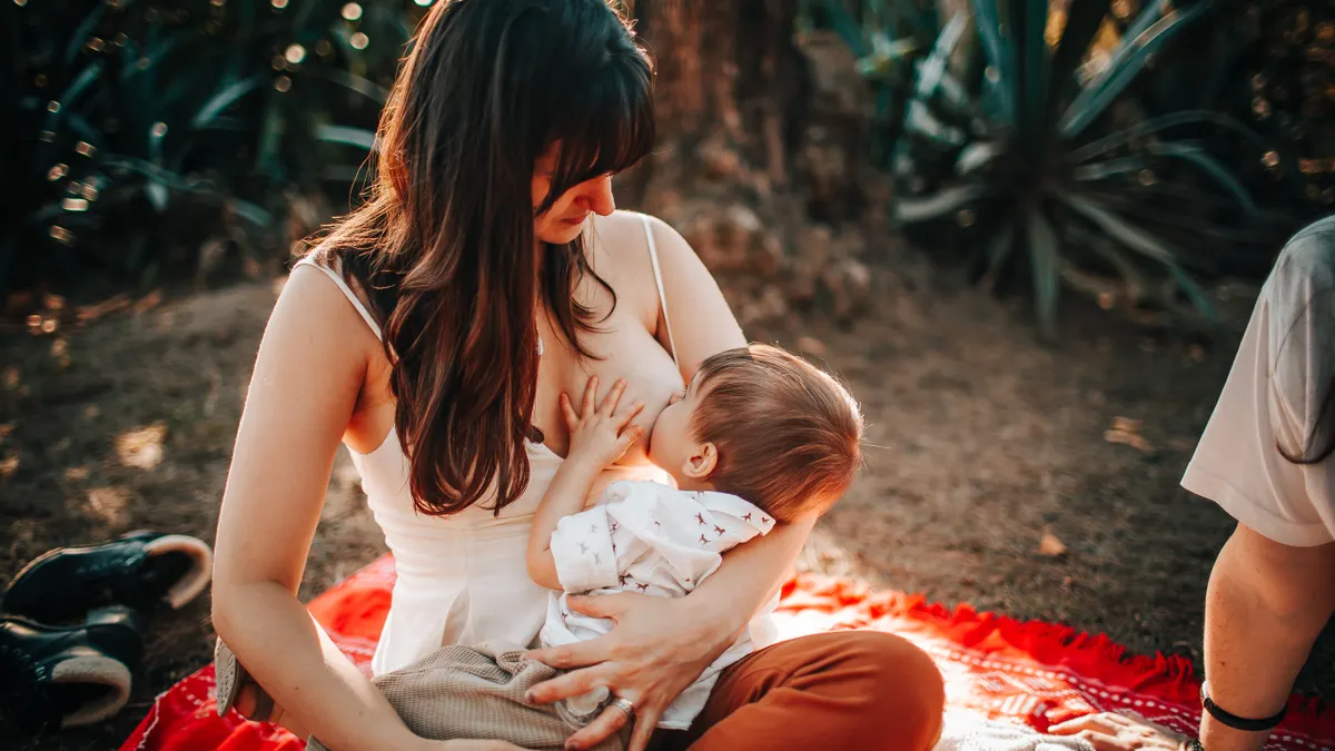 woman breastfeeding a baby outdoors on a blanket