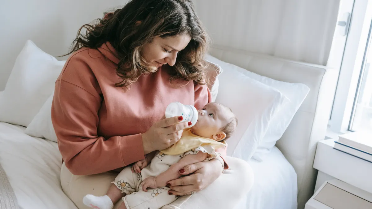 mother bottle-feeding a baby on a chair