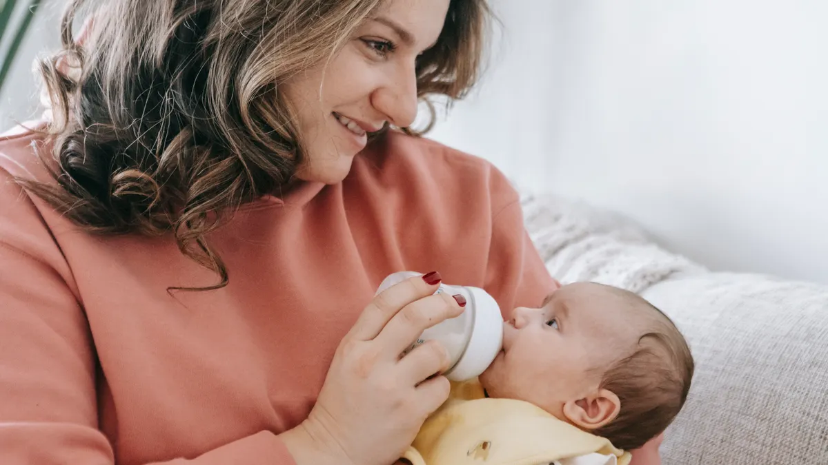 mother bottle-feeding a baby on a couch