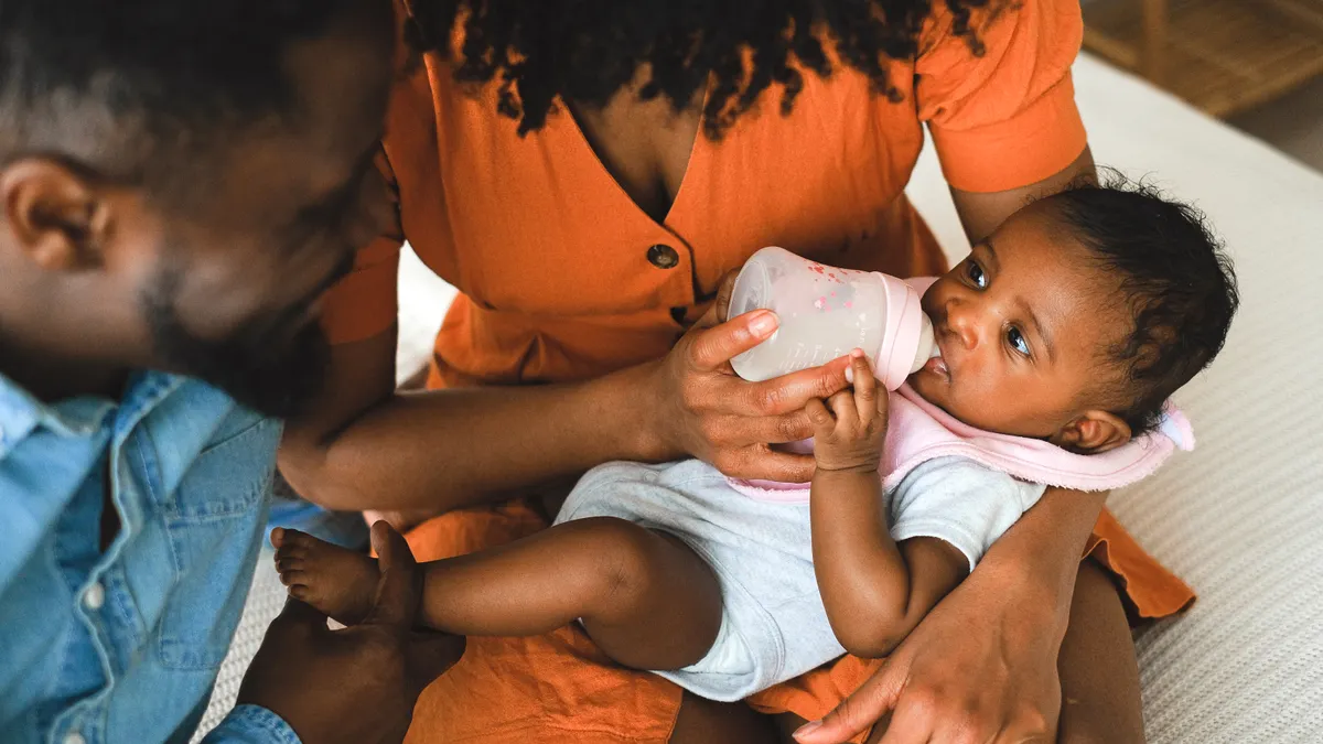 Parents bottle-feeding a baby on a couch